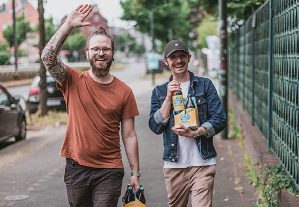 Eine Glasflasche mit Bier, kondensbedeckt und verschlossen, trägt ein gelbes Etikett mit blauen Blumen.