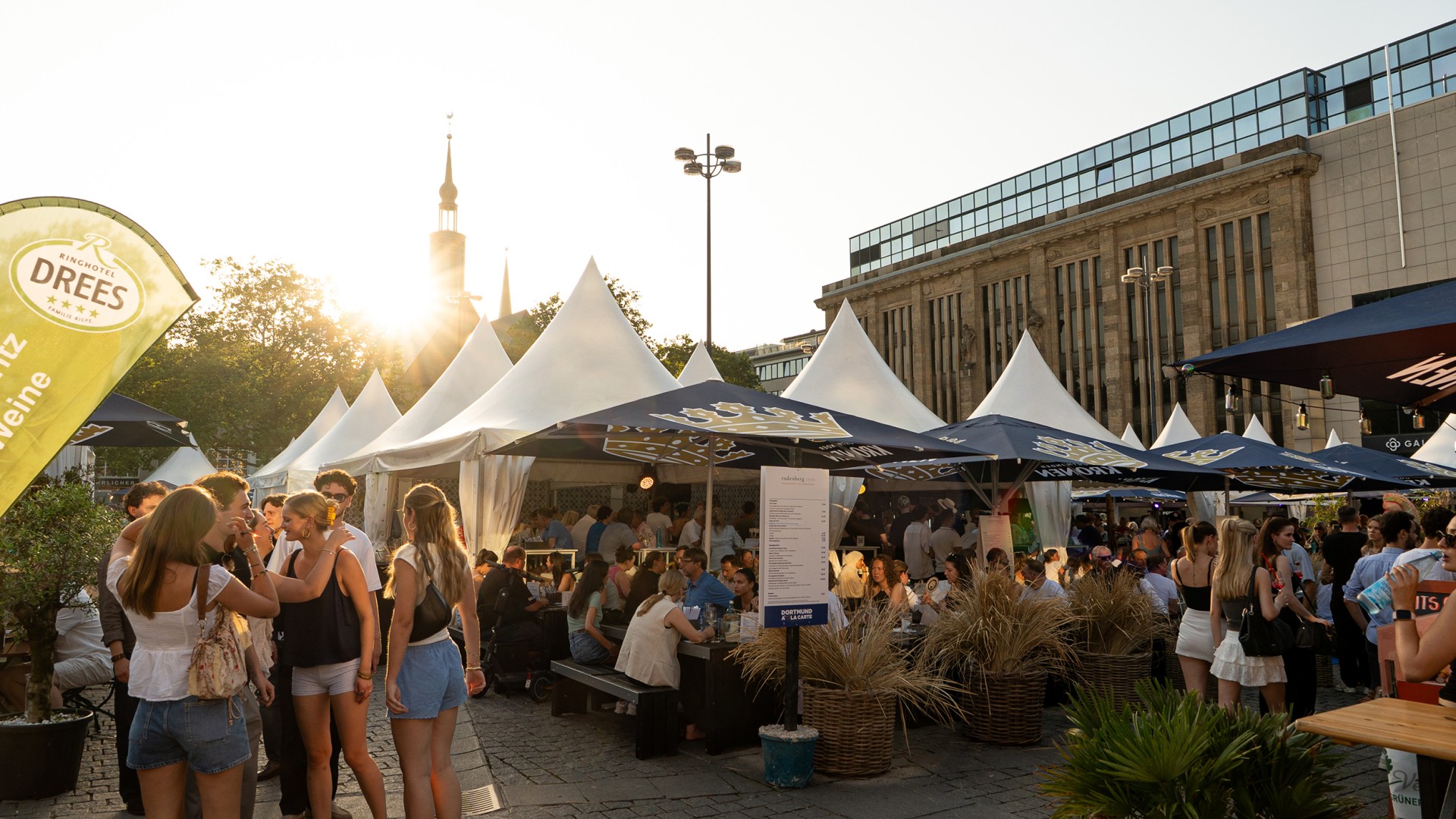 Menschen sitzen unter Sonnenschirmen auf dem Dortmund á la Carte Festival auf dem Hansaplatz.