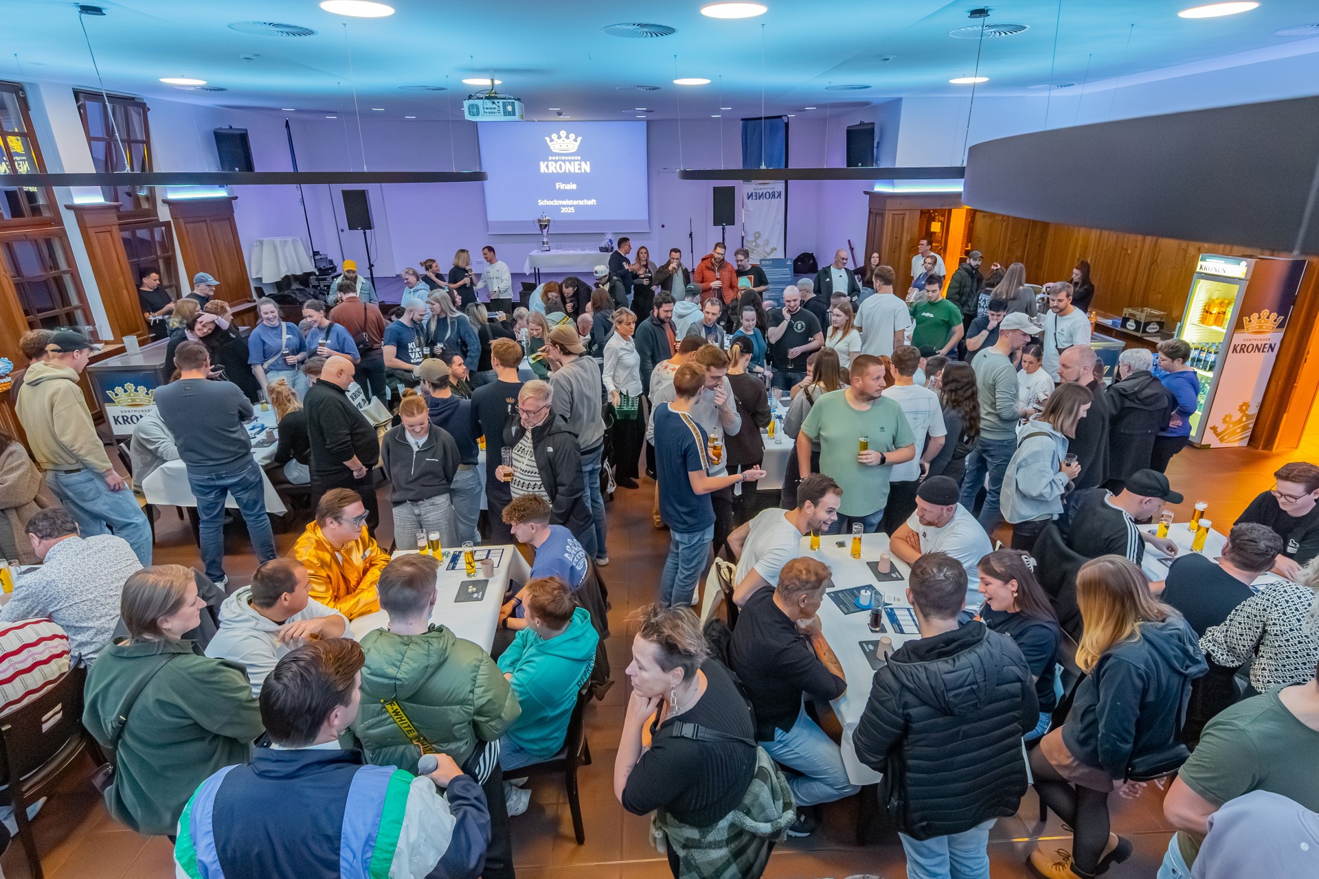 Ein großer Saal ist mit vielen Personen gefüllt. Hinten in der Mitte wird eine Präsentationsfolie mit den Worten 