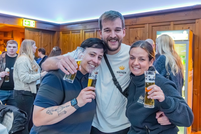 Drei Personen umarmen sich und halten jeweils ein Glas mit Bier der Marke Dortmunder Kronen hoch.