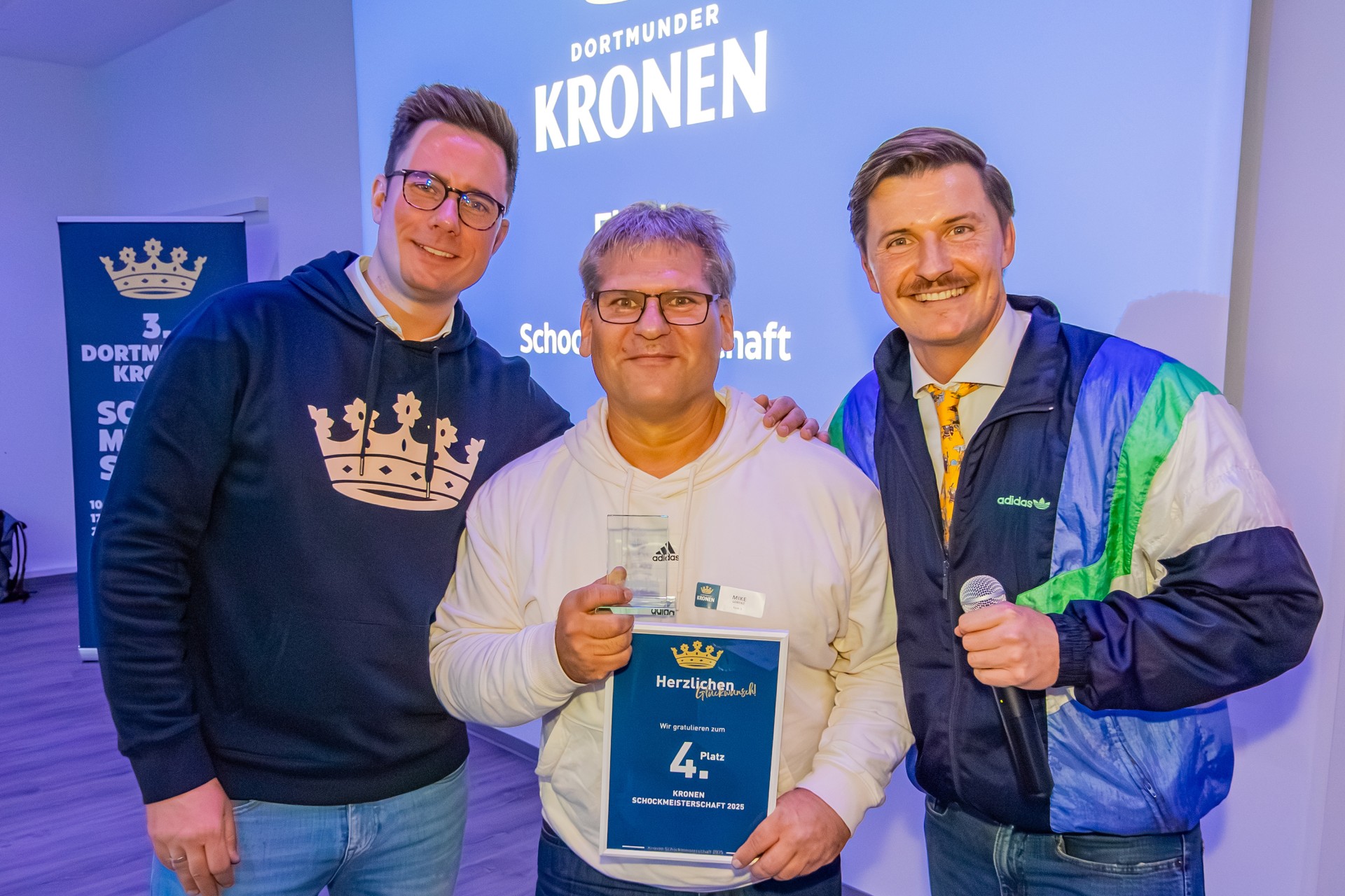 Drei Männer stehen nebeneinander. Der Mann in der Mitte hält eine Glastrophäe und eine Urkunde mit den Worten 