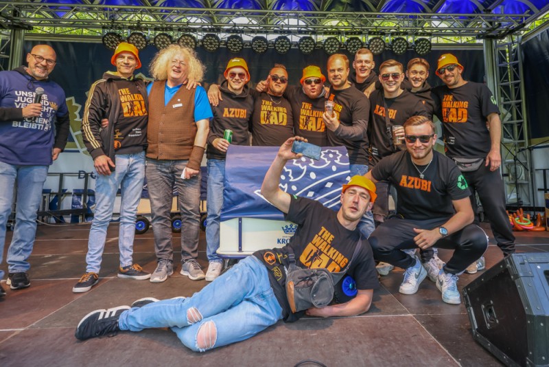 Gruppe von Männern in verschiedenen Freizeitoutfits posiert lächelnd auf einer Bühne.