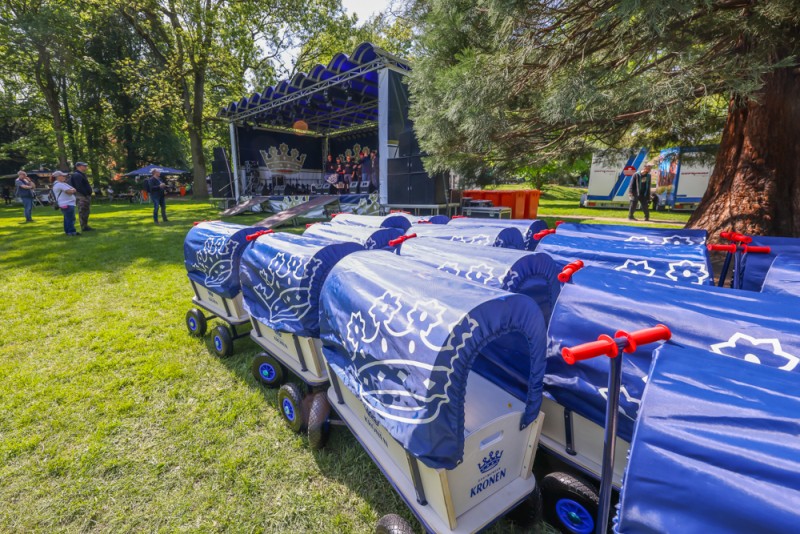 Mehrere blaue Bollerwagen stehen auf einer Wiese nahe einer Bühne im Park.