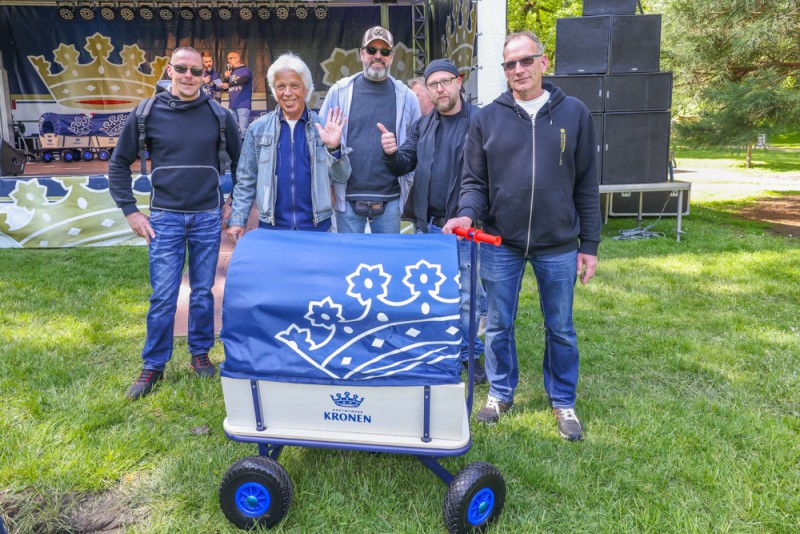 Vier Männer stehen auf einer Wiese neben einem blauen Bollerwagen.