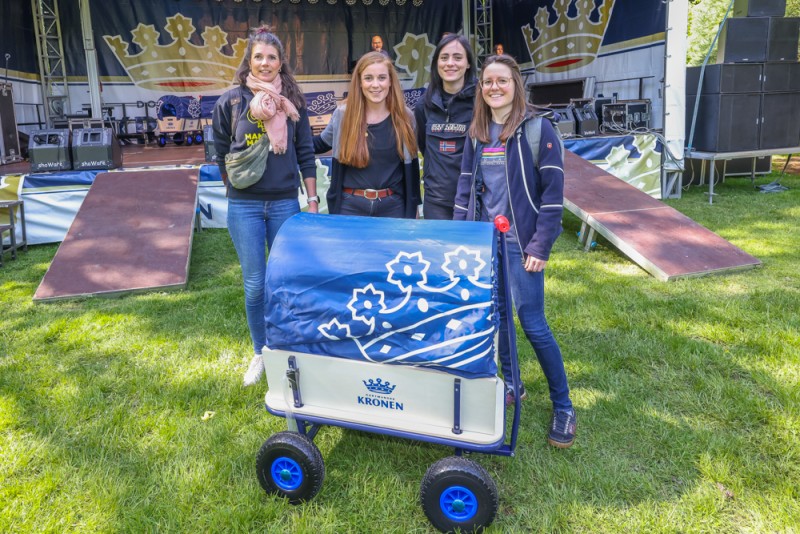Vier Frauen stehen lächelnd neben einem blau bedruckten Wagen auf einer Wiese.