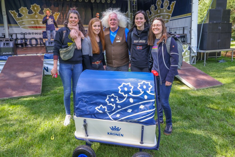 Fünf Personen stehen lächelnd neben einem bedruckten Wagen im Freien.