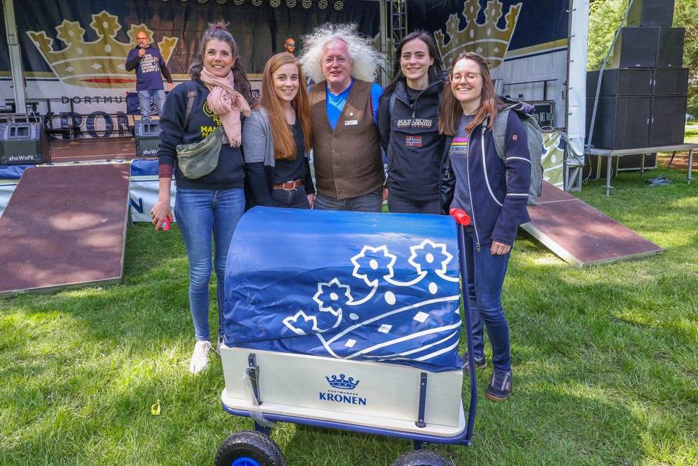 Fünf Personen stehen lächelnd neben einem bedruckten Wagen im Freien.