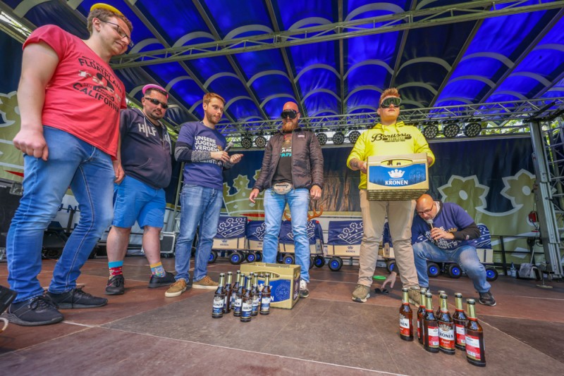 Sechs Männer stehen auf einer Bühne mit Getränkekisten und Flaschen darunter.