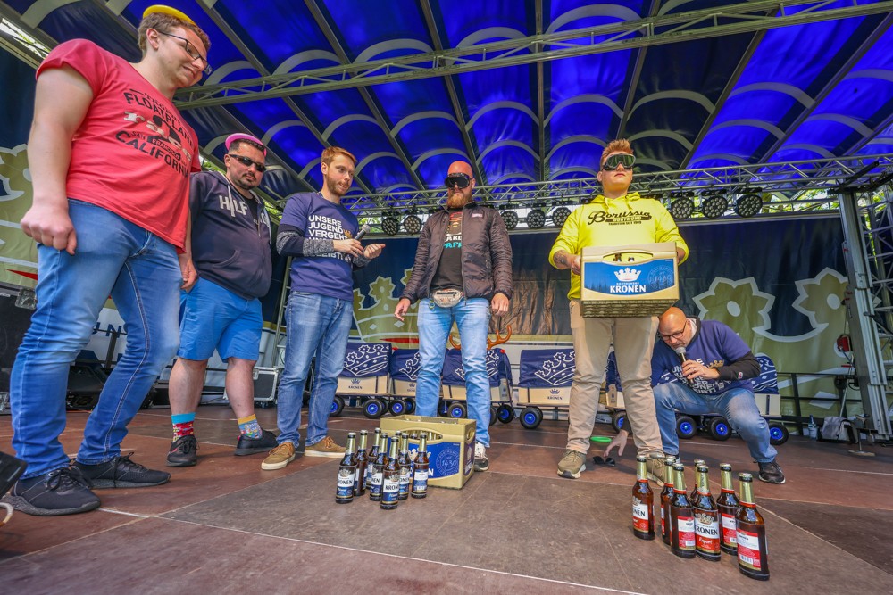 Sechs Männer stehen auf einer Bühne mit Getränkekisten und Flaschen darunter.