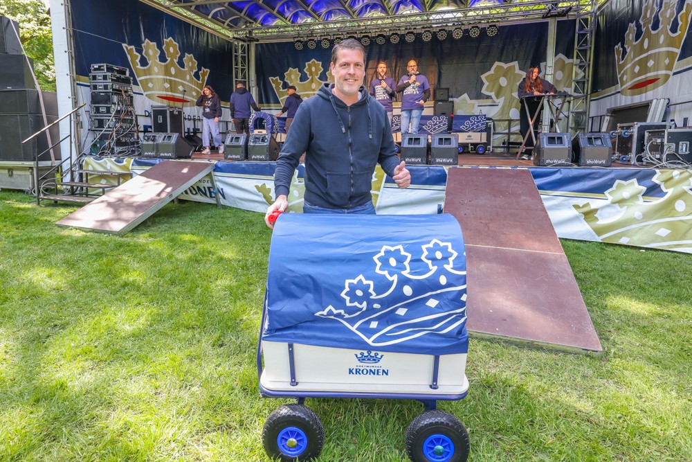 Ein Mann schiebt einen blauen Handwagen vor einer Bühne mit Musikern.