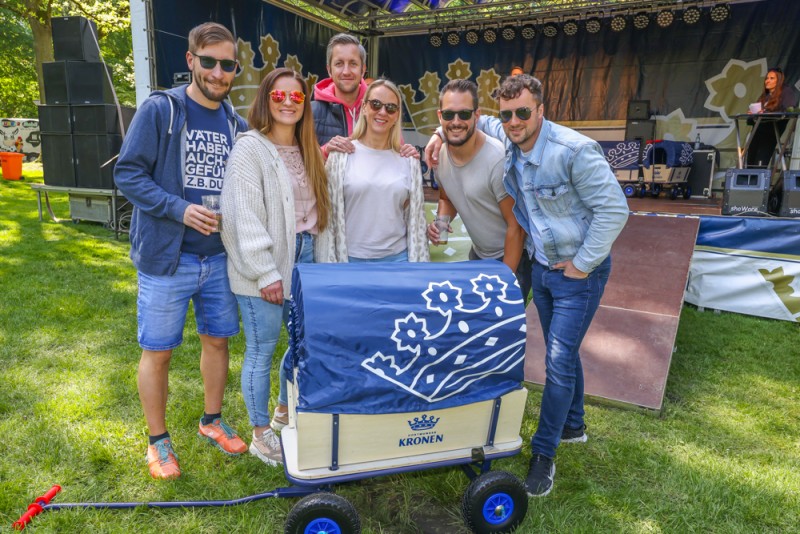 Drei Männer und zwei Frauen stehen lächelnd neben einem blau dekorierten Handwagen.