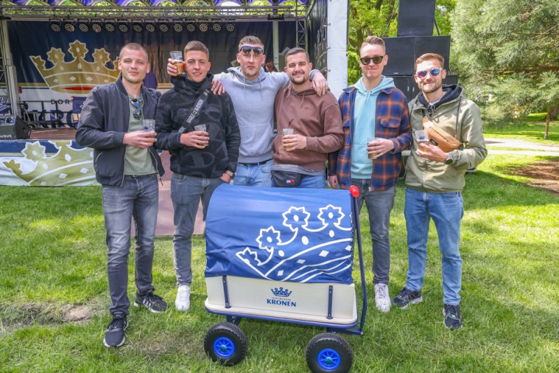 Sechs Männer stehen lächelnd draußen mit einem Getränkewagen auf einem Festival.