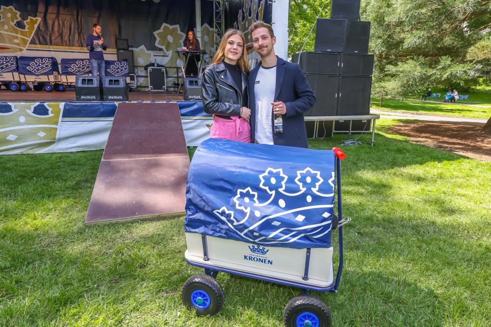 Ein Mann und eine Frau stehen lächelnd neben einem Wagen in einem Park.