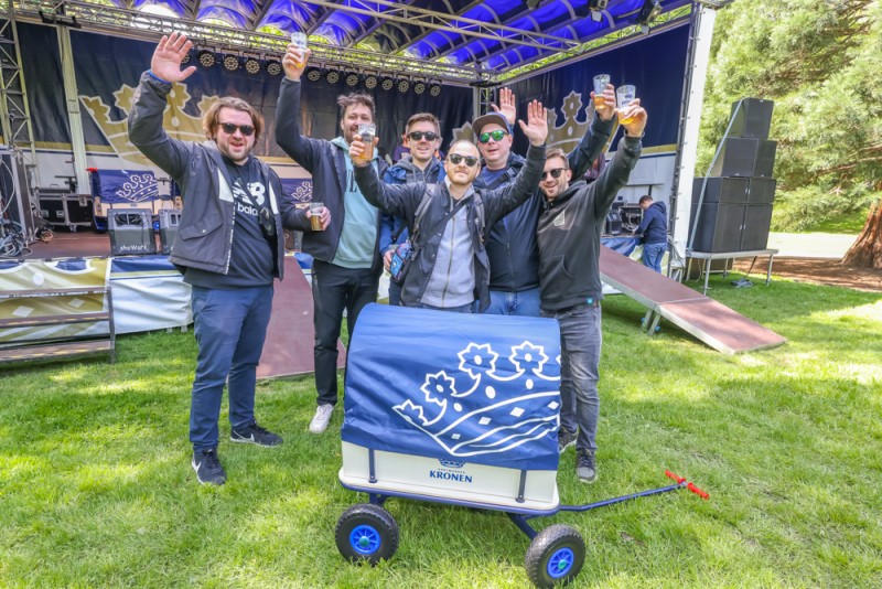 Fünf Männer heben vor einer Bühne im Park die Arme und halten Biergläser hoch.