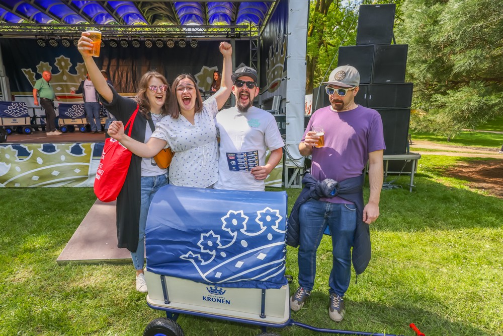 Vier Erwachsene feiern ausgelassen bei einem Fest im Freien neben einem geschmückten Wagen.