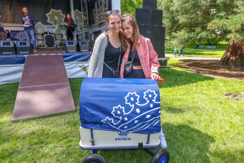 Zwei Frauen lächeln neben einem blau dekorierten Wagen auf einem Festival.