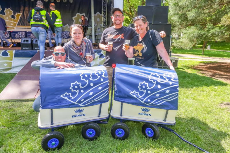 Vier Personen stehen lächelnd im Freien neben zwei blau-weißen Bollerwagen.