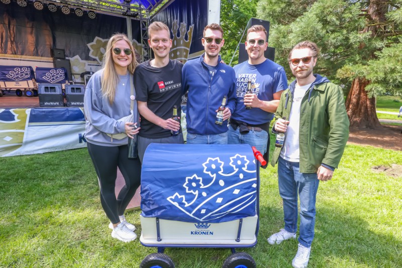 Fünf Personen stehen lächelnd neben einem kleinen Wagen in einem Park.