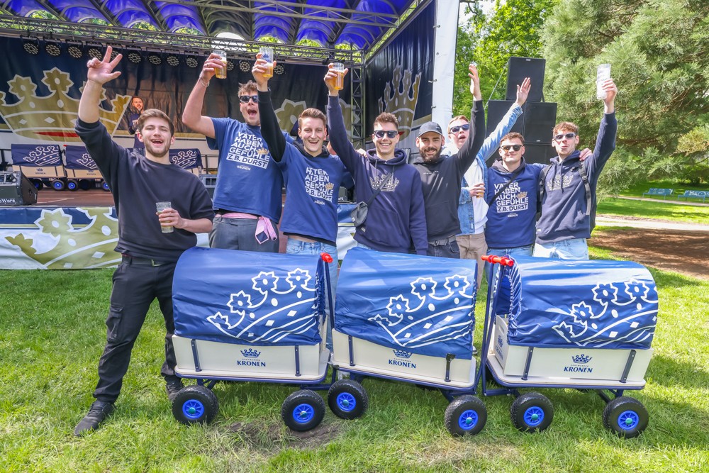 Mehrere Männer in blauen Oberteilen feiern ausgelassen im Freien, einige heben Getränke hoch.