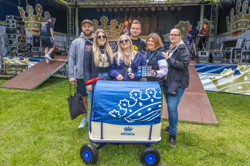 Sechs Personen stehen lächelnd neben einem Wagen auf einer Veranstaltung im Freien.