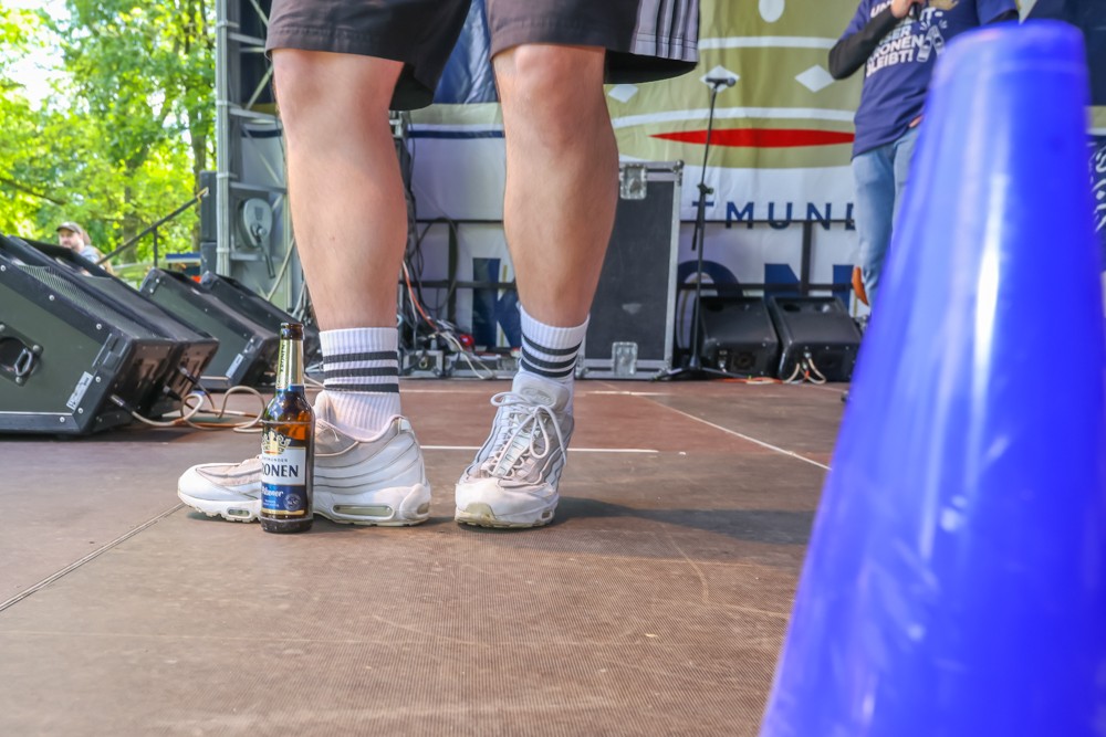 Zwei Paar Beine in Sportschuhen stehen auf einer Bühne neben einer Bierflasche.
