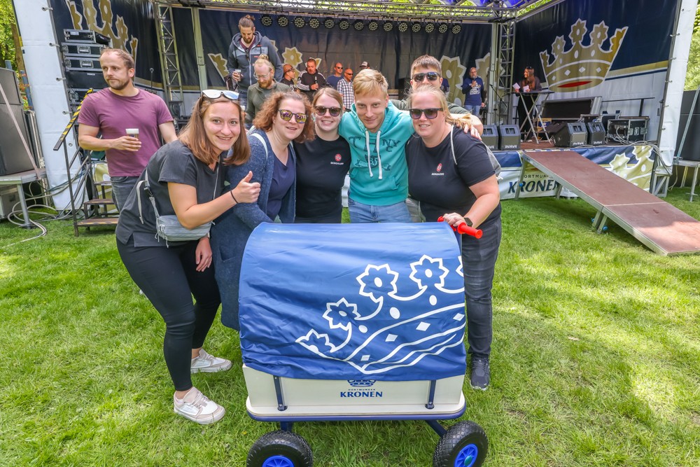 Fünf Personen lächeln neben einem blau bedeckten Wagen bei einem Outdoor-Event.