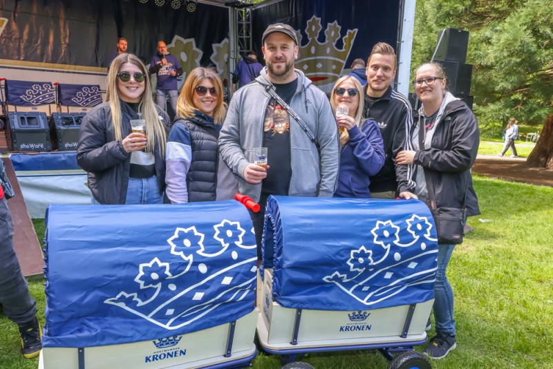 Drei Paare stehen lächelnd vor einer Bühne mit Musikinstrumenten und halten Getränke.
