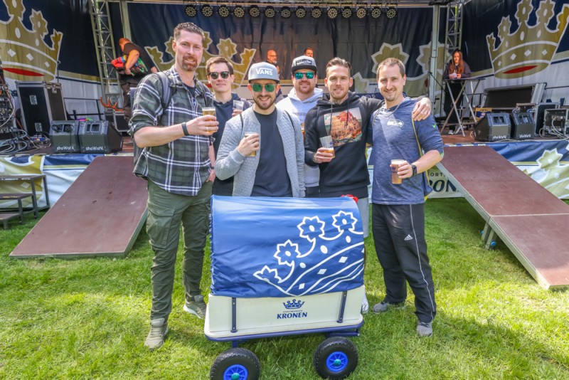 Gruppe von sechs Männern steht lächelnd mit Getränken auf einem Musikfestival.
