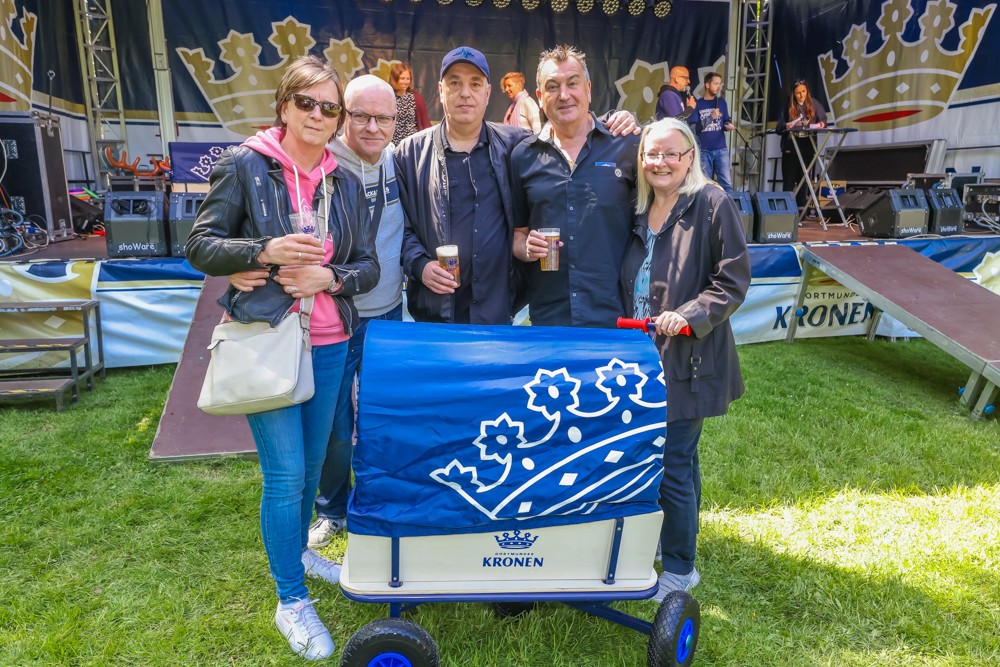 Fünf Erwachsene stehen lächelnd vor einer Bühne mit einem blau dekorierten Wagen.
