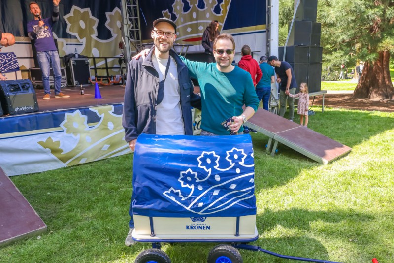 Zwei Männer stehen lächelnd vor einer Handkarre auf einem Festival.