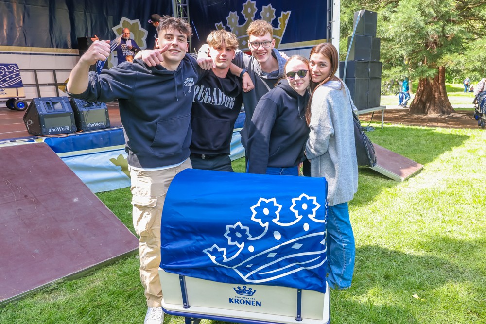 Fünf junge Menschen stehen lächelnd vor einer Bühne und halten eine blaue Flagge.