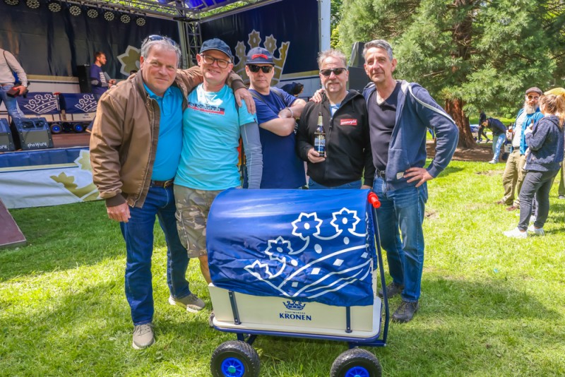 Vier Männer stehen lächelnd im Freien neben einem blauen Wagen.
