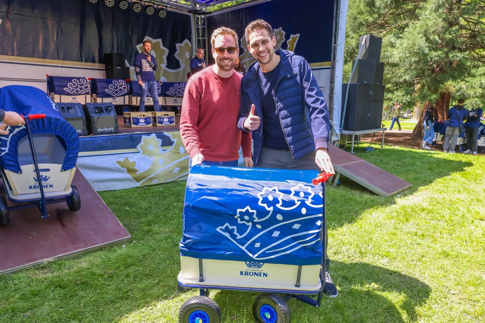 Zwei Männer stehen lächelnd vor einer Bühne und halten einen Wagen.