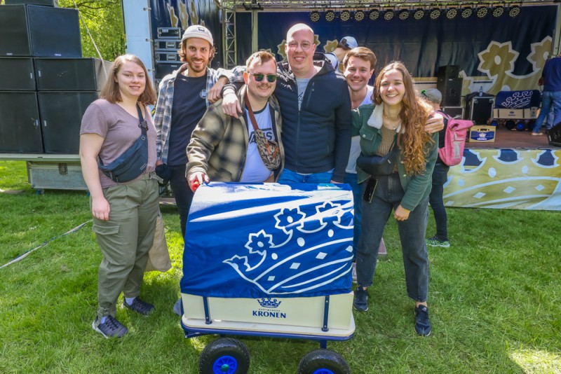 Sechs Personen stehen lächelnd hinter einem blau verzierten Wagen im Park.