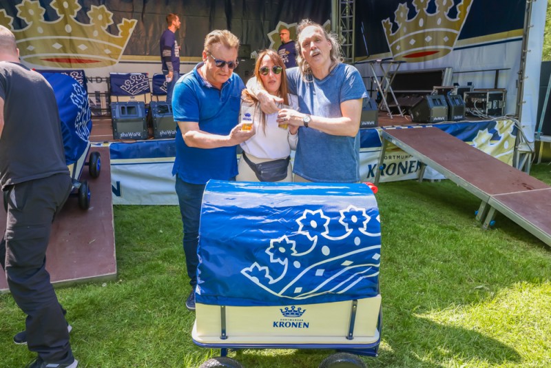 Drei Personen stehen lächelnd an einem geschmückten Wagen bei einem Outdoor-Event.