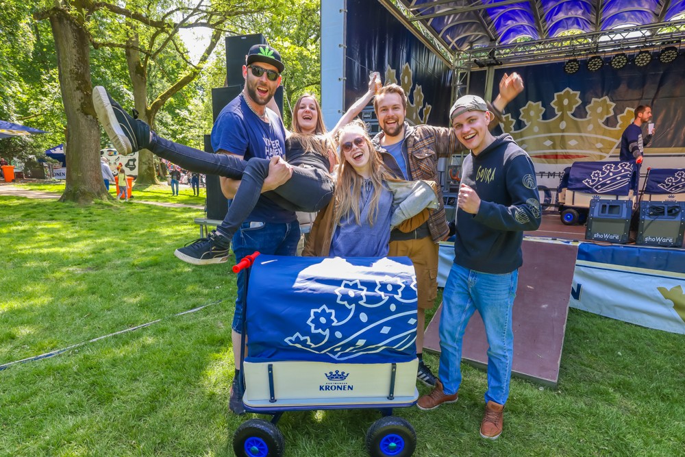Fünf fröhliche Menschen posieren auf einem Festival neben einem dekorierten Wagen.