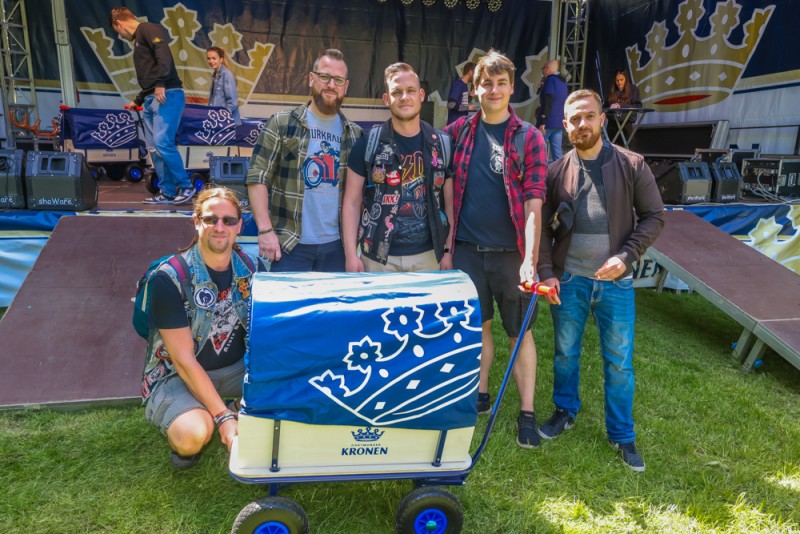 Fünf Männer stehen lächelnd hinter einem blauen Wagen auf einer Bühne.