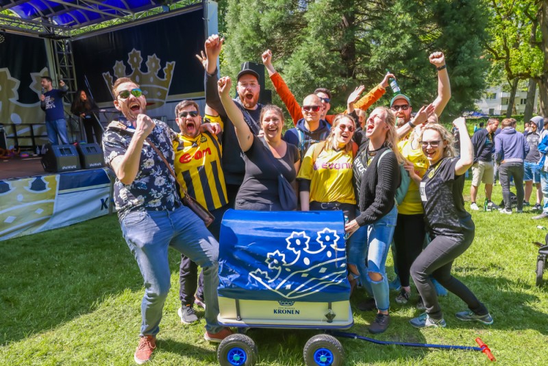 Eine Gruppe aufgeregter Menschen jubelt im Freien vor einer Bühne. Sie umarmen sich und zeigen energische Gesten.