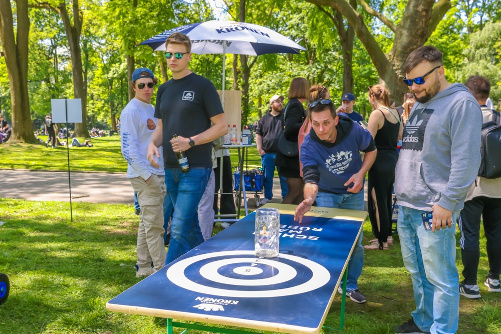 Männer spielen Tischspiel im Park, einer wirft einen Beutel auf die Zielplatte.