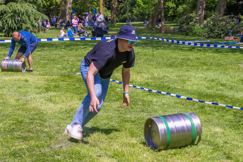Ein junger Mensch in blauem T-Shirt rennt mit einem glänzenden Fass in einer Wettbewerbsumgebung im Park.