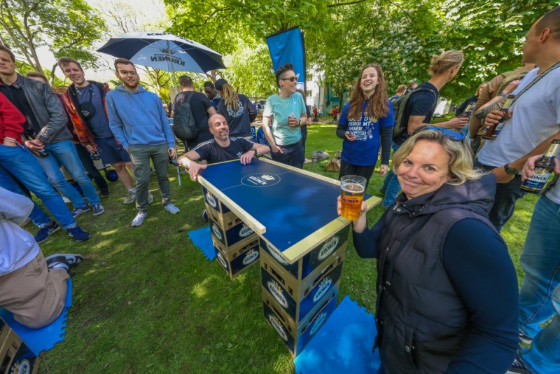 Eine Gruppe von Menschen genießt ein Tischtennisspiel im Freien bei sonnigem Wetter.