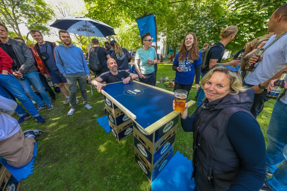 Eine Gruppe von Menschen genießt ein Tischtennisspiel im Freien bei sonnigem Wetter.