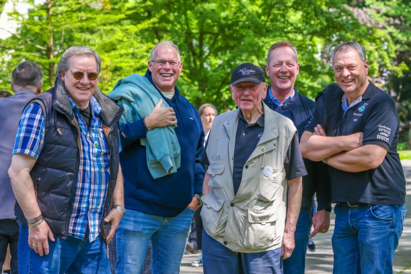 Fünf lächelnde ältere Männer stehen draußen in einer Gruppe zusammen.