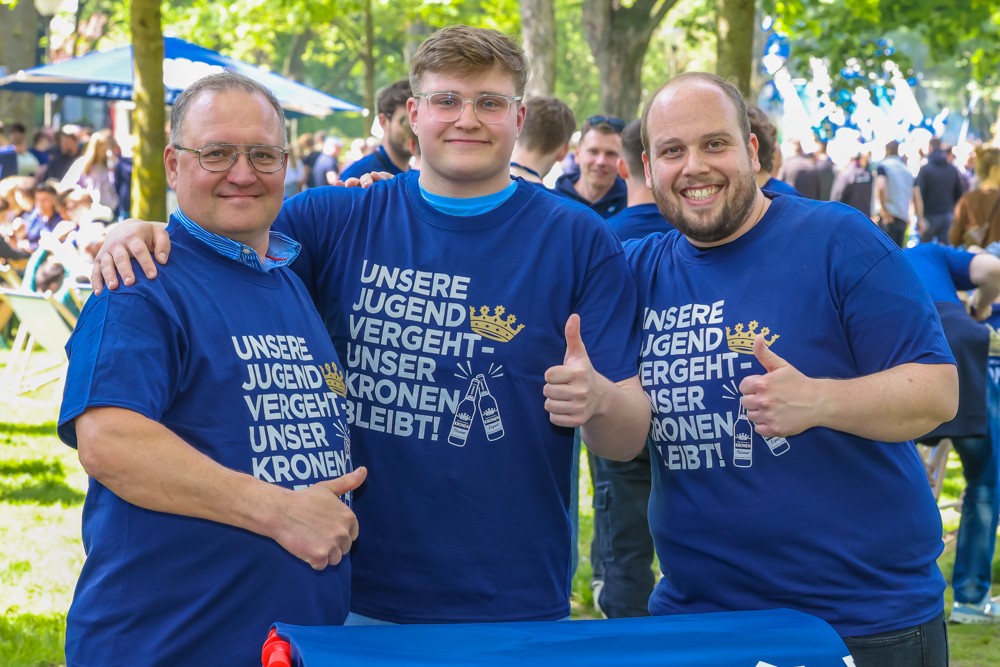 Drei Männer in blauen T-Shirts lächeln und posieren im Freien.
