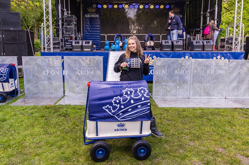 Eine Person steht mit einem Kronen Bollerwagen vor einer Bühne und macht das Victory Zeichen.