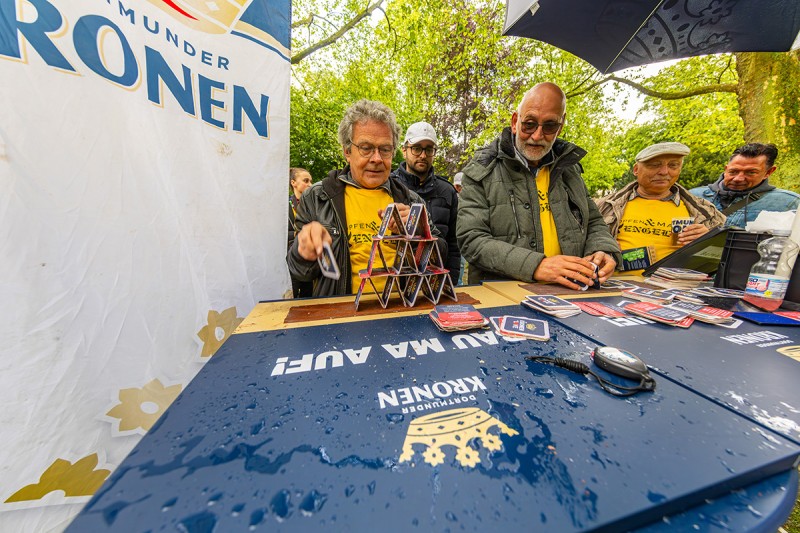 Zwei Personen bauen eine Kartenhaus aus Dortmunder Kronen Bierdeckeln im Freien.